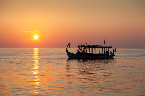 Maldivian typical seascape with sunset and a dhoni, a Maldivian local nautical vessel.
