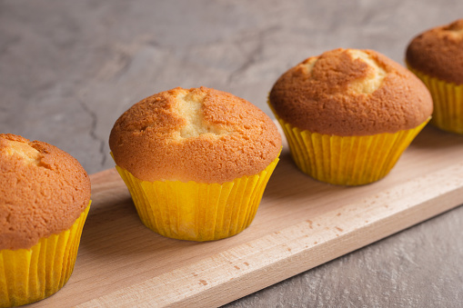 Freshly baked vanilla muffins on wooden board on dark stone table. Selective focus. Homemade food.