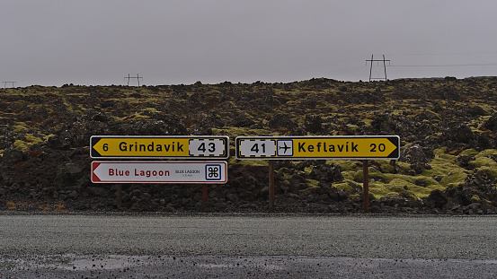 Grindavík, Reykjanes, Iceland - 03-19-2021: Directional signs at junction of rural road between lava fields showing the direction to tourist resort Blue Lagoon, Grindavik village and to Keflavík.