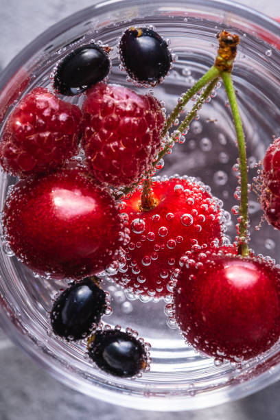 istock Fresh cold sparkling bubble water drink with cherry, raspberry and currant berries in transparent glass on stone concrete background, summer diet beverage, top view macro 1317249118