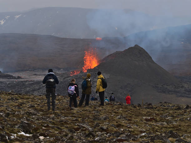 Astonished people watching lava explosion of volcanic eruption at Fagradalsfjall mountain with women pointing on the volcano with smoke. stock photo