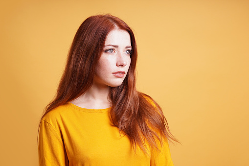 young woman with blank expression contemplating thought - yellow background with copy space