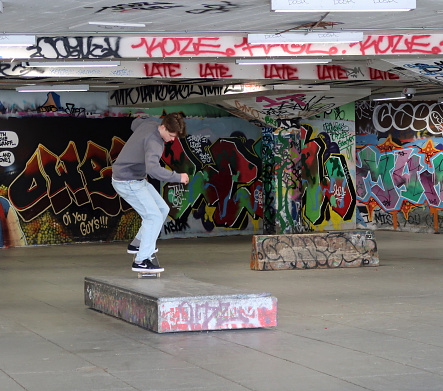Young adult white male doing skateboard tricks. Graffiti covered concrete Skateboard and BMX park or space beneath Royal Festival Hall, London River Thames Southbank. London, United Kingdom, May 4,2021