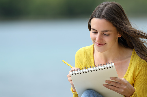 Happy woman drawing in a notebook in a lake