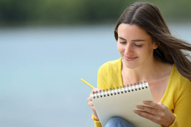 happy woman drawing in a notebook in a lake - nature writing women ideas imagens e fotografias de stock