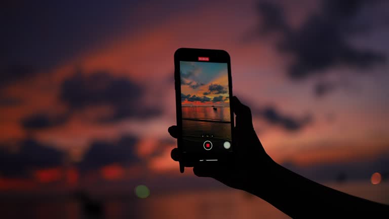 Woman's hand recording the sunset beach view on smart phone