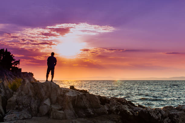 istock Man Standing On Rock By Sea Against Sky During Sunset 1317269269