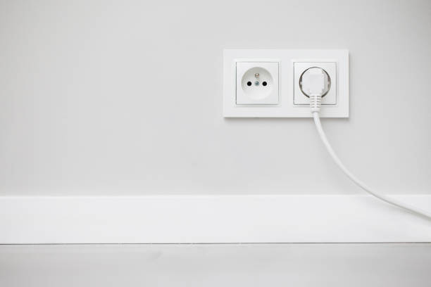 istock Electrical socket isolated on gray wall. White wire plug plugged in. Renovated studio apartment power supply background. 1317273299