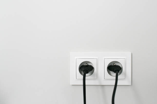 istock Brand new electrical socket isolated on gray wall. Black wire plug plugged in. Renovated studio apartment power supply background. 1317273658