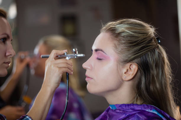 artista femenina rociando maquillaje en el ojo de una modelo femenina en el estudio - airbrushing fotografías e imágenes de stock