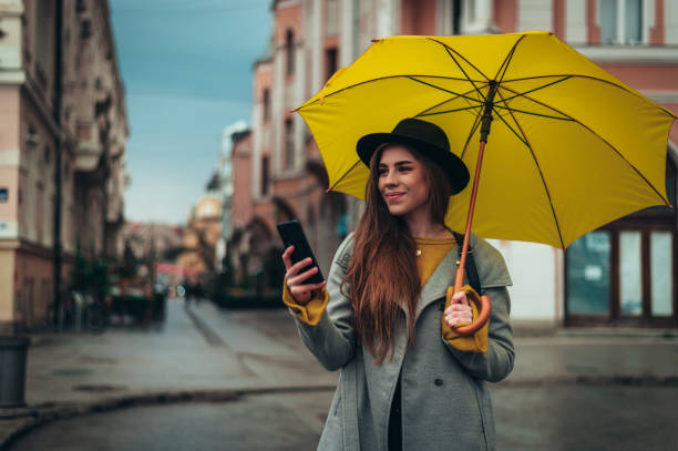 istock Woman using a smartphone while holding a yellow umbrella outside 1317275036