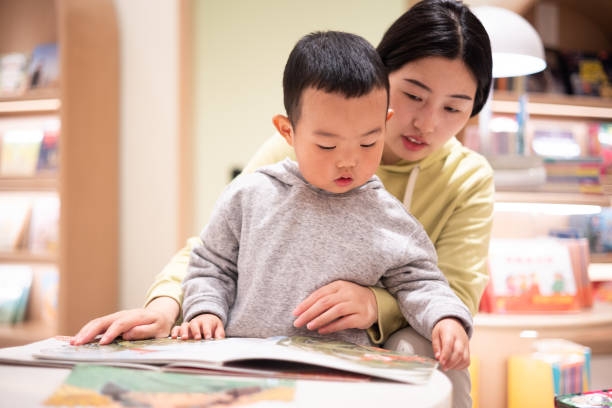 mãe com menino lendo livro na biblioteca - picture book library preschool bookshelf - fotografias e filmes do acervo