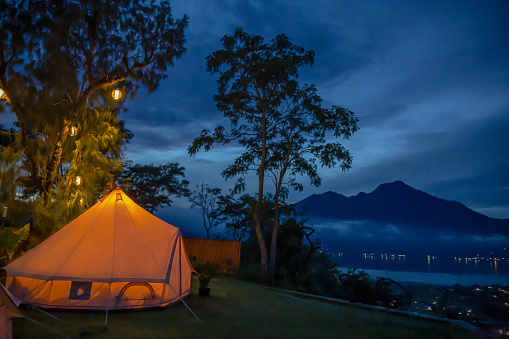 Shot of illuminated tent in a romantic glamping site at night with Mount Batur view.