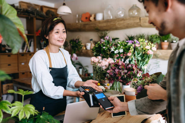 buona coppia che fa shopping al negozio di fiori. il giovane asiatico che paga per un bouquet con il suo smartphone, scansiona e paga una fattura su una macchina da carta effettuando un pagamento contactless facile e veloce. tecnologia nfc, concetto tap an - florist telephone flower business foto e immagini stock