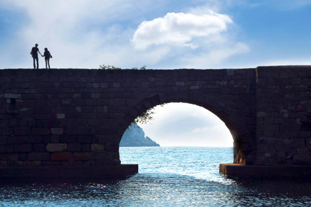 Young woman in a blue swimsuit swimming in calm water beneath a historic stone bridge arch. Outdoor nature scene with rocky cliffs and greenery. Relaxing moment in a natural setting.