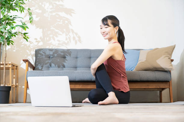 A woman doing yoga while looking at the computer screen A woman doing yoga while looking at the computer screen in the room yoga instructor stock pictures, royalty-free photos & images