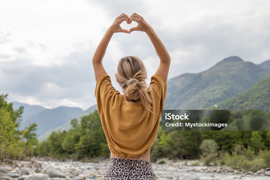 Young woman loving nature, she makes heart with hands She stands on a rock by the river, forest and mountains on background.
Ticino canton, Switzerland Heart Shape Stock Photo