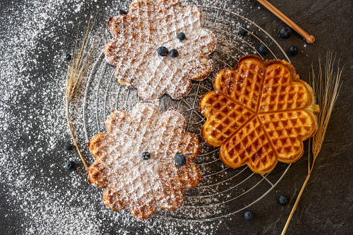 homemade fresh baked heart shaped waffles with powdered sugar on a cooling rack on dark table background