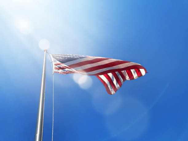 istock Waving American flag at tall flagpole over sunny blue sky 1317285565