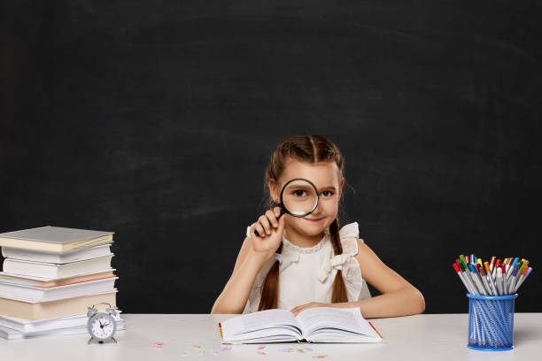 istock cute schoolgirl sitting at table with magnifying glass 1317287336
