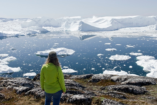 A woman explores the Ilulissat Icefjord area in Greenland during spring. Awe inspiring solo travel at a UNESCO World Heritage Site.