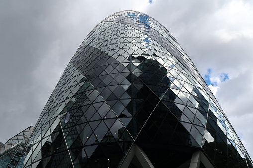 Skyscraper tower the Gherkin in city of London financial district. Bottom to top close up diminishing perspective. Outdoors on a cloudy day. London, United Kingdom, May 4, 2021