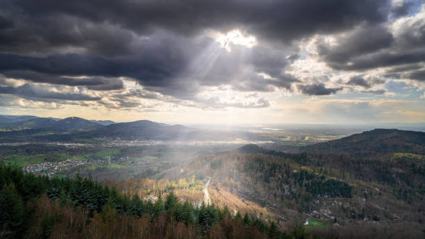 The sun shines through the clouds on a road in the black forest
