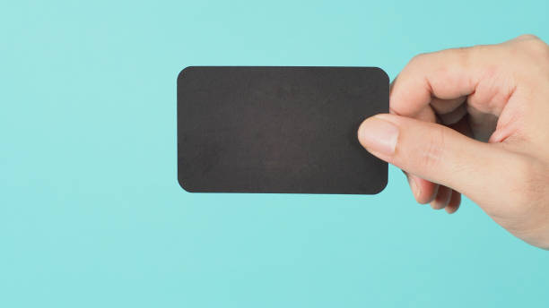 istock Empty space for text.Male hand holding black blank card isolated on mint green or Tiffany Blue background. 1317296598