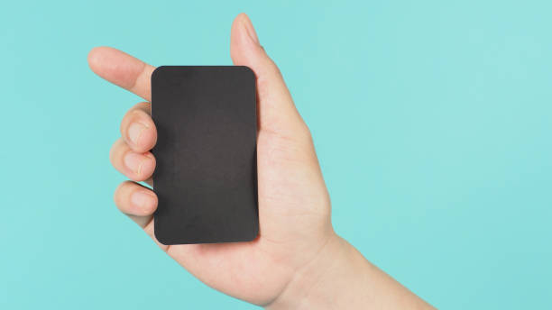 istock Empty space for text.Male hand holding black blank card isolated on mint green or Tiffany Blue background. 1317296599