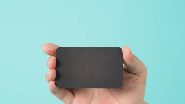 istock Empty space for text.Male hand holding black blank card isolated on mint green or Tiffany Blue background. 1317296600