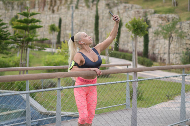 woman resting after an exercise, standing on the bridge and looking in distance while listening music on headphones