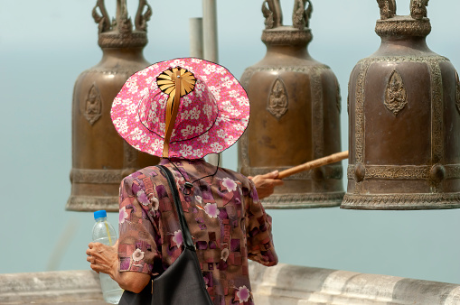 hua hin thailand may  5 - 2006  -  an unknown woman in hua hin walks by a temple area and with a wooden stick strikes large metal bells