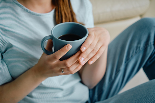 Unrecognizable woman drinking coffee while relaxing on the sofa at home.