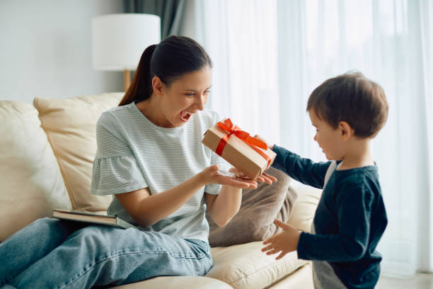 Cheerful mother receiving a present from her small son at home.