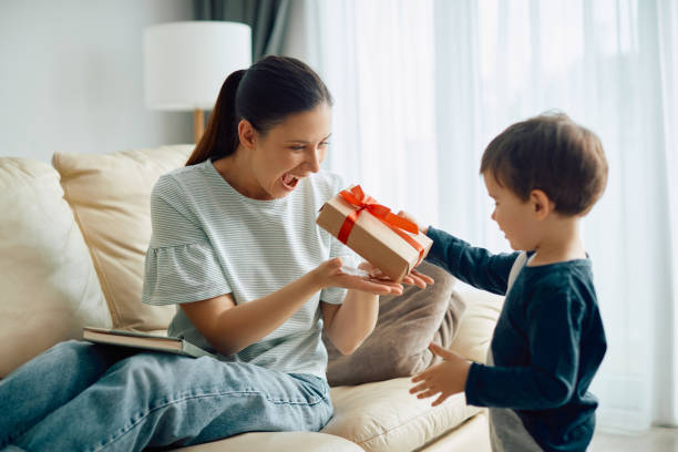 cheerful mother receiving a present from her small son at home. - mother gift imagens e fotografias de stock