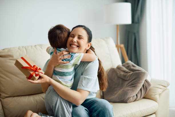 istock Happy mother embracing her son while receiving a gift box from him at home. 1317303262
