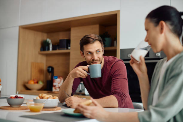 istock Smiling couple talking while eating breakfast together at dining table. 1317303325