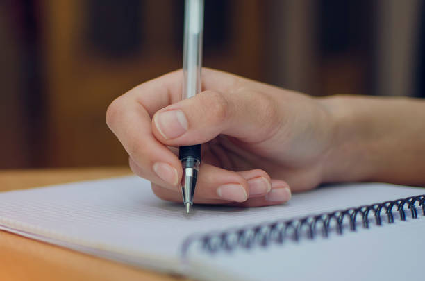 istock Close up of woman's hands writing spiral notepad placed on wooden work table 1317305524