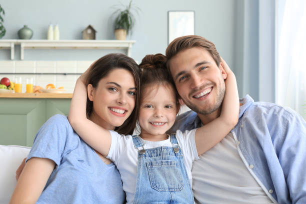 istock Positive friendly young parents with smiling little daughter sitting on sofa together while relaxing at home on weekend. 1317306033