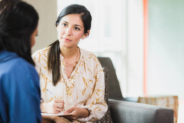 Caring counselor listening to female patient An attentive counselor listens and takes notes as a vulnerable patient discusses an important topic. empathy stock pictures, royalty-free photos & images