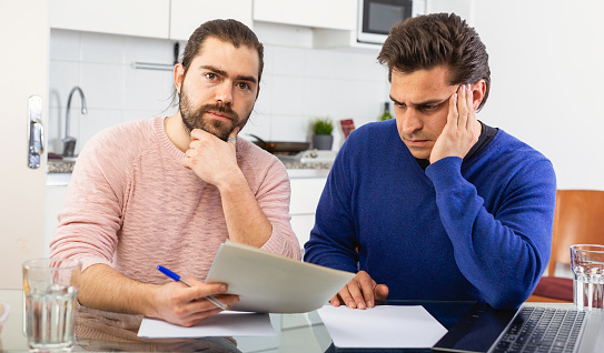 Man having problems with some documents; worriedly discussing with friend at home table