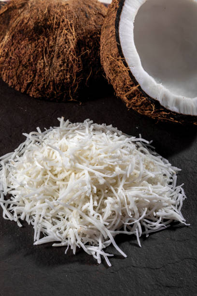 Open coconut in the middle on top of stone with coconut shavings and grated coconut