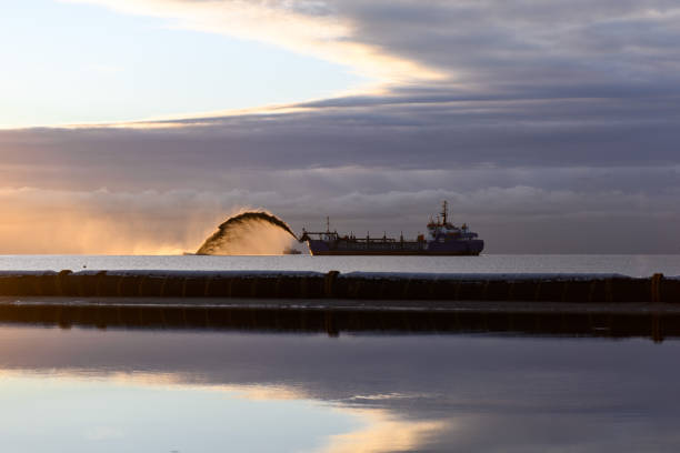 Vessel engaged in dredging at sunset time. Hopper dredger working at sea. Ship excavating material from a water environment. Beautiful sunset. stock photo