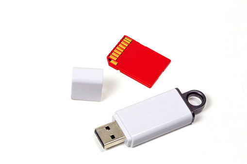 The USB Thumb Drive, or Memory Stick and an SD Memory Card is shot on a white background. The device itself is white and the cap is also pictured off to the side. The SD Card is red. This Computer storage device has a subtle shadow and is a great technology object that is easily clipped out of the background.