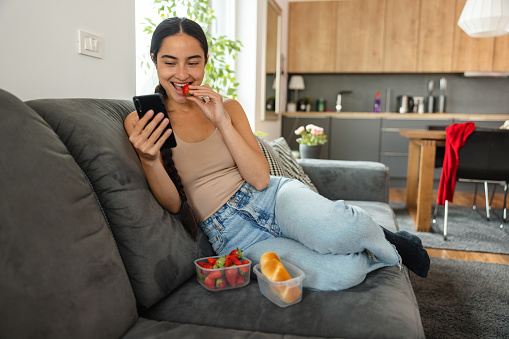Beautiful Woman Eating Fruits And Using Smart Phone On The Sofa