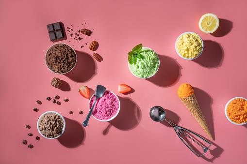 Assorted ice cream cups and waffle cones colorful different flavor as chocolate, mango, strawberry, mint, vanilla, lemon, coffee, nuts on pink background