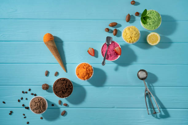 istock Assorted ice cream cups in a row and waffle cones colorful on blue wood background 1317328084