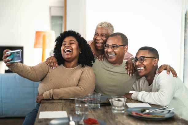 Happy black family having fun taking selfie with mobile smartphone cam while having lunch at home