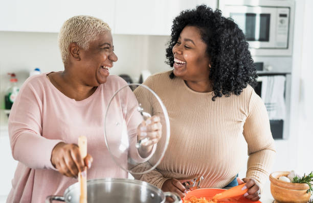 happy afro mother and daughter preparing lunch together in modern house kitchen - food and parents unity concept - family american culture african culture black imagens e fotografias de stock