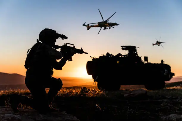 Battlefield with a soldier, armored vehicle and flying helicopters at sunset